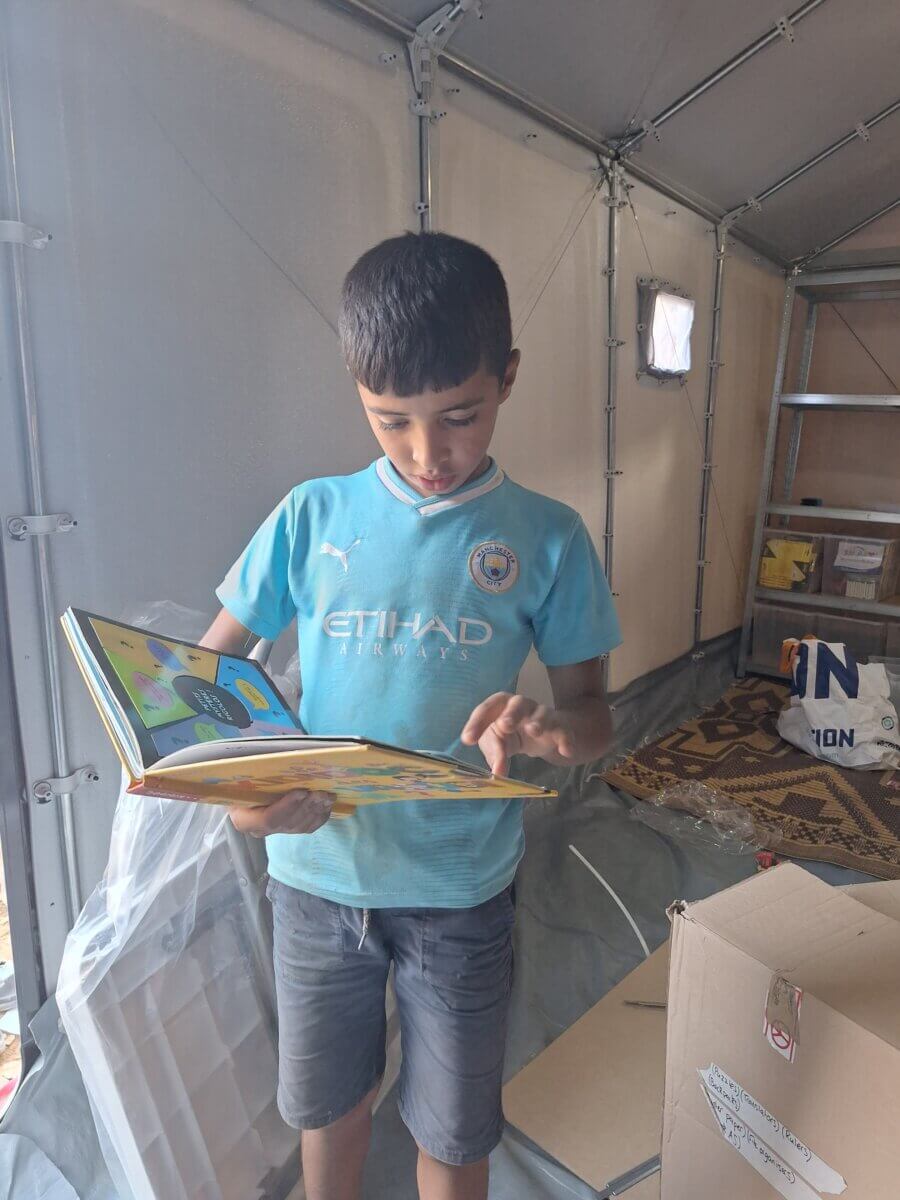 A boy reads a book at a community library set up in one of the relief housing units installed by People for People